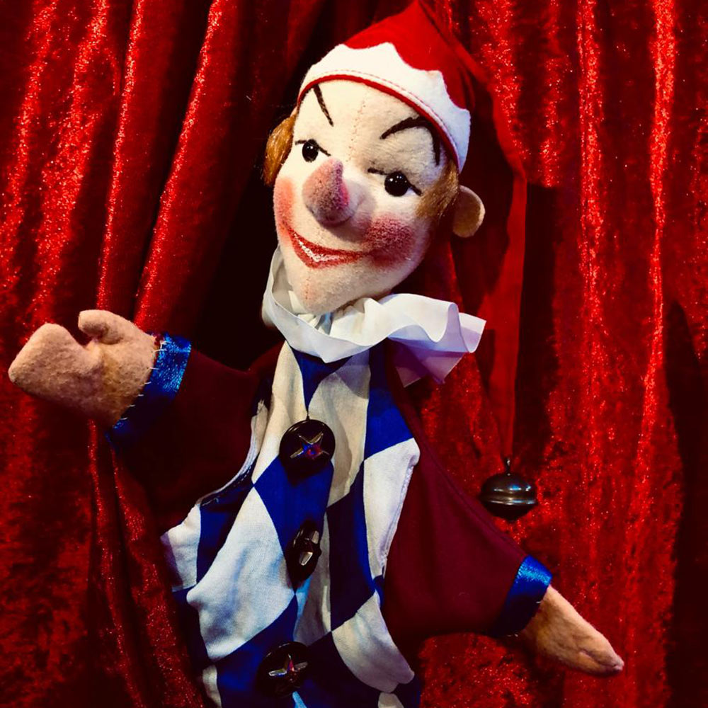 Die Puppe Kasperl vom Kasperltheater Blumenschein vor rotem Vorhang Die Puppe Kasperl vom Kasperltheater Blumenschein vor rotem Vorhang